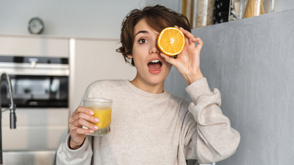 Eine junge Frau hält ein Glas Orangensaft in der Hand.