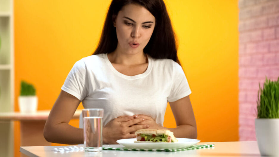Eine Frau hält sich aufgrund von Magen-Darm-Beschwerden den Bauch und nimmt gerade eine kleine Zwischenmahlzeit zu sich.