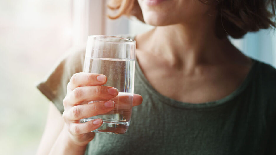 Eine junge Frau hält ein Glas Wasser in der Hand. 