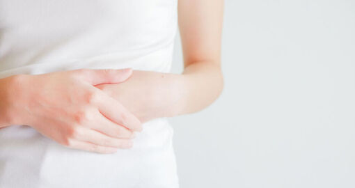 Eine Frau hält sich die Hände auf den Bauch aufgrund ihrer Magen-Darm-Beschwerden.